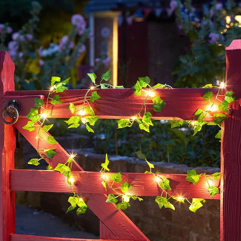 Decorative string lights with green leaves on a red wooden gate at night.