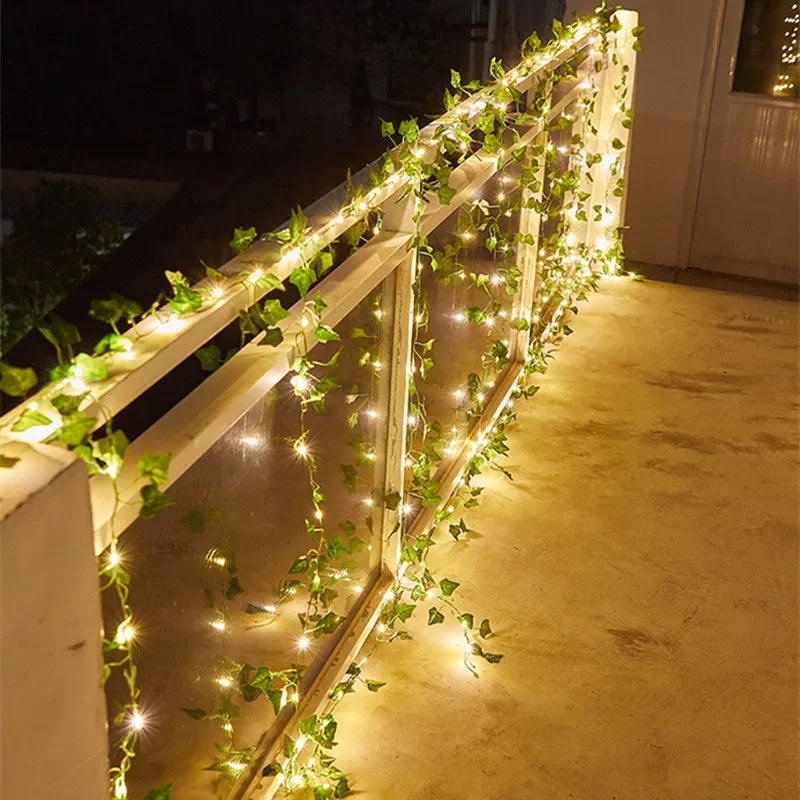 Decorative string lights and greenery on a railing at night.