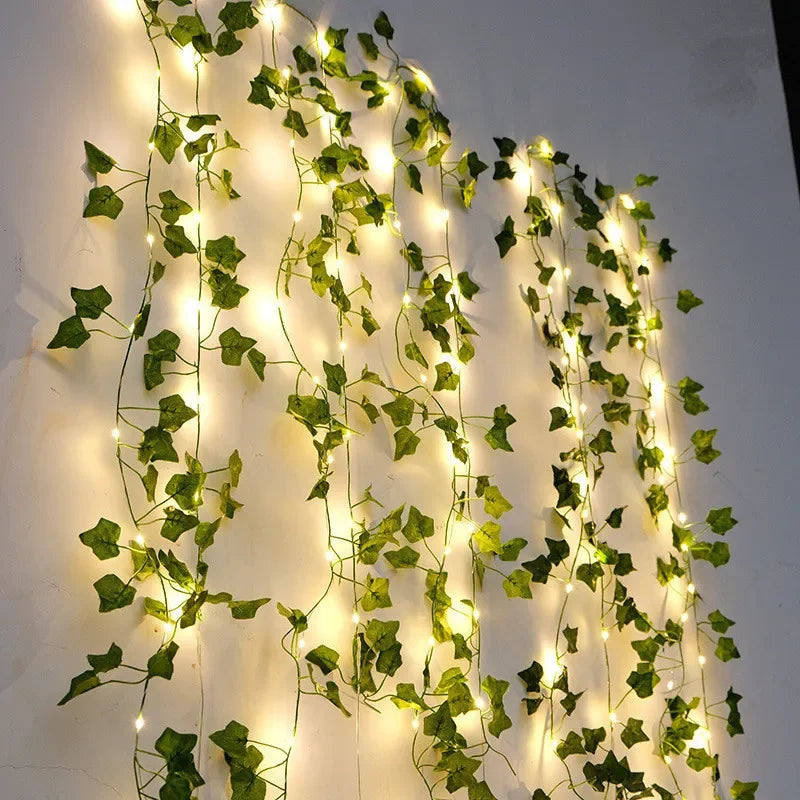 Green ivy wall lights with warm white LED fairy strings draped vertically on a plain white wall.